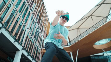 Kameraya bakan beyaz sokak dansçısının portresi. Genç, çekici bir adam, modern alışveriş merkezinde hip hop gösterisi yapıyor. Düşük açı. Serbest stil dansı. Açık hava sporu 2024. Hiphop.
