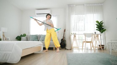 Gülümseyen kulaklıklı hizmetçi yerleri temizlerken müzik dinliyor. Oturma odasında dans ederken yerleri paspaslayan Kafkasyalı mutlu bir anne. Gülümseyen anne ev işi yapıyor. Yaşam tarzı. Pedagoji