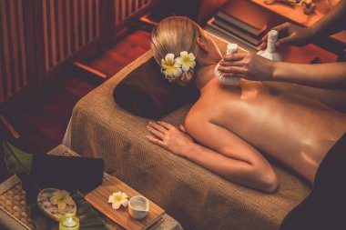 Sıcak bitkisel top spa masaj vücut tedavisi, masör kadın vücuduna nazikçe şifalı bitki torbası bastırıyor. Aromaterapi tesisinin sakinliği ve dinginliği kaplıca salonundaki mumların sıcacık ışığında. Sessiz.