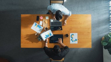 Erkek lider, pazarlama ekibi tablet üzerinde çalışırken ve mali tablolara bakarken grafiği analiz etmek için dizüstü bilgisayar kullanıyor. Başlangıç grubunun çözüm bulma ve birlikte plan yapma stratejisinin en üst görünümü. Cemaat.