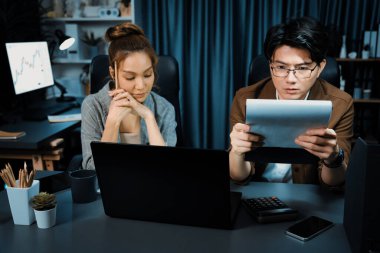 Stresli suratlı iki yönetici birlikte evrak işlerini tartışıyorlar. Modern ofiste gece geç saatlerde dizüstü bilgisayarla karşılaştırıldığında şirket projesinde çalışıyorlar. İnfobahn.