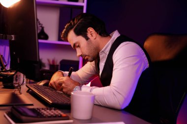 Stresli akıllı işadamı, kağıt işleri üzerine not pazarı verileri yazarak, gece geç saatlerde mor neon karanlık aydınlatma odasındaki disiplin ürünü hizmetlerinin çevrimiçi satış kanalını analiz ediyor. Tahmin et..