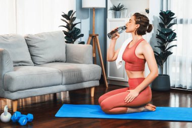 Sportif ve atletik kadınlar spor paspası üzerinde su içiyorlar. Vücut egzersizlerini bitirdikten sonra evde sağlıklı fiziğe ve spor yaşam tarzına uygun bir yaşam sürüyorlar. Gaiety evde egzersiz eğitimi.