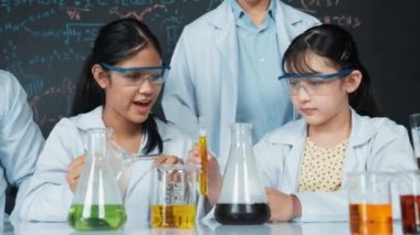 Zeki öğretmen, çeşitli deneyler yapan çocuklara destek olur ve onlarla ilgilenir. Karışık ırktan lise öğrencisi masadaki biyokimyasal sıvıyı mikroskop ile inceliyor. Öğretim