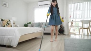 Modern evde müzik eşliğinde yerleri paspaslayan sevimli bir kız. Temizlik eldivenli enerjik kız ev işi yapıyor ve şarkı söylerken yatak odasını temizlemekten zevk alıyor. Yaşam tarzı. Pedagoji.