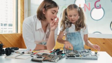 Genç, zeki, beyaz bir öğretmen öğrencilere elektronik kurulun bir parçasını öğretiyor. Uzman kız dijital elektrikli aletleri öğreniyor ve cips ve kablolarla ana kartı tamir ediyor. Etkinlik.