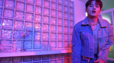 Çekici Asyalı sanatçı parlak neon ışıkta adım atıyor. Kameraya özgüvenle bakarken serbest stil müzikle dans eden yakışıklı break dans. Profesyonel hippi rahatla. Mutluluk.