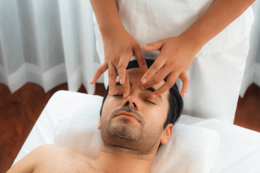 Beyaz adam stres önleyici kafa masajından ve lüks bir tatil beldesi veya otel spa salonundaki modern ışık ortamında yüz güzelliği eğlencelerini şımartmaktan hoşlanıyor. Sessiz.