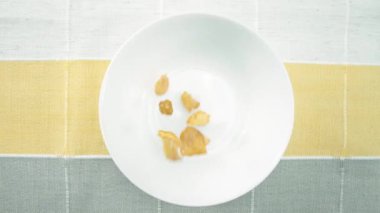 Sağlıklı sarı bir mısır gevreğinin bovlinge düşüşünü. Mısır gevreğinin beyaz ve siyah arka planda beyaz kaseye düşüşünün yukarıdan görünüşü. Makrografi. Ağır çekim. Kahvaltı konsepti. Pabulum.