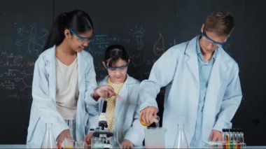 Zeki çocuk deney yaparken deney kabında sıvı karıştırıyor. Akademik öğrenci laboratuvar önlüğü giyerken masada mikroskop ve deneysel ekipmanlarla renkli örnekler koyuyor. Öğretim