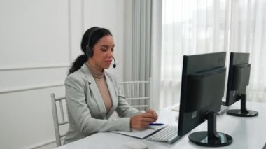 İş kadını kulaklık takıyor ve uzaktan müşteri ya da iş arkadaşını desteklemek için ofiste çalışıyor. Çağrı merkezi, tele pazarlama, müşteri destek acentesi telefon görüntülü konferans görüşmesi için hayati önem taşıyor.