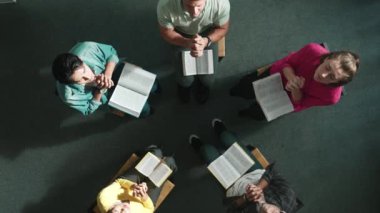 Katlanmış eller yaparken, kucağında haçla İncil okuyan duaların en üstteki görüntüsü. İnanç, güven ve umutla Tanrı 'ya dua eden farklı insanların havadan görünüşü. Ve daireler çizerek oturuyor. Sempozyum.