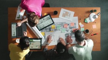 İnşaat mühendisi ekibi toplantıda beklerken yapışkan nota bakıyor. Tasarımcının çalışmasına ve notlara bakmasına ilişkin en üst görünüm, meslektaşı açıklama yaparken ve birlikte çalışırken planda yer alıyor. Sempozyum.