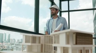 Gökdelen manzarasına bakarken yürüyen profesyonel mimar mühendisi. Masaya yerleştirilmiş ev modeliyle pencereye bakarken yetenekli proje yöneticisi proje planını tutuyor. Tasarım. İzleme