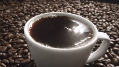 Kahve ya da kahve çekirdekli espresso manzarası. Taze kavrulmuş kahve çekirdeğini yakın çekimde ahşap masanın etrafına bir fincan americano ve aromatik akarsu ve tohum dumanı serpin. Geliştirilebilir.