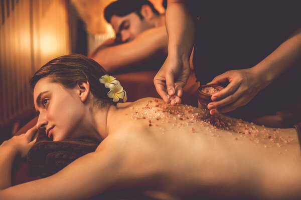 Пара клиентов, проводящих пилинг в роскошном спа-салоне с теплым свечой окружающей среды. Косметическое лечение бальзамическим скрабом в Health spa scrub. Quiescent