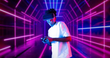 Neon soyut arka planda oyun oynarken elinde joystick tutan ve VR gözlük takan bir genç. Afrikalı adam kontrol etmeyi ve artırılmış gerçeklik teknolojisini kullanmayı seviyor. Yaratıcılık.