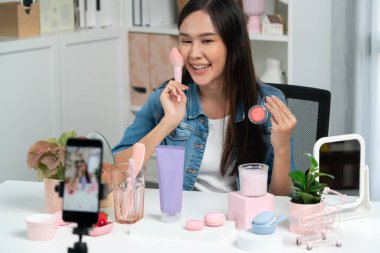 Genç, güzel Asyalı makyaj fırçası yanak testi koleksiyonunu pastel renkle inceliyor. Sosyal medyada akıllı telefonu tanıtmak için pembe ile ışıltılı bir ruh hali sergiliyor. Taktik.