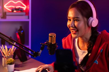 İnternet üzerinden kulaklık takıp gülümseyen Asyalı güzel kız flamasının sunucu kanalı izleyicilerle internet üzerinden konuşma yapıyor. Esport yetenekli takım oyuncuları neon mavi odada. Taktik.