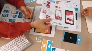 Mobil uygulama için kullanıcı arayüzü prototipini ofis çalışanlarına sunan harika bir şirket çalışanı. UX UI tasarımcısı kağıt üzerinde simge tasarımının işlevini açıklıyor. Sinerjik