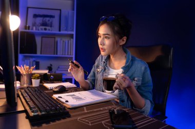 Elinde kahve fincanıyla bilgisayara bakan Asyalı güzel yaratıcı bir kadının iş piyasası grafik klasörü raporuna gece vakti işaret ettiğini düşünmek. Taktik.