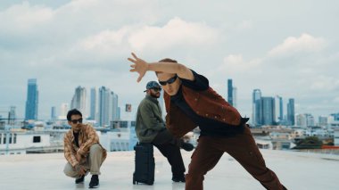 Bir grup profesyonel hip hop dansçısı çatıda break dans yapıyor. Becerikli koreograf serbest stil hareketini gösterirken, arkadaş da cesaretlendirir, alkışlar, alkışlar. Açık hava sporu 2024. Hiphop.