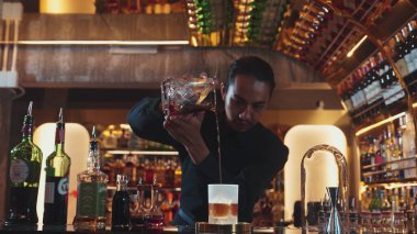 Asyalı barmen soğuk bardağa karışık viski dökerek soğutmalı buzlu içecek üretiyor. Lüks ılık barlarda alkol yenileme gösterisine odaklanan yaratıcı bir reklam yapıyor. Vinosity.
