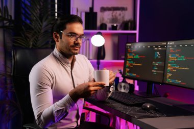 Akıllı IT geliştiricisi, bilgisayar ekranında yazılım geliştirme kodlu kahve fincanı tutuyor. Dışarıya bakıyor, program güncellemesi internet sitesi verilerini neon ışıklı siber ofiste sunuyor. Tahmin et..
