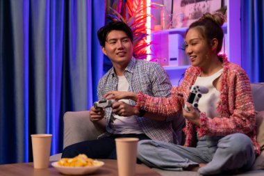 Neşeli, gülümseyen bir çiftin koltuğunda oturup oyun oynuyorlar. Oyun konsolu, hazır aperatifler ve içecekler, modern neon ışıklı, rahat oturma odasında eğlenceli bir rekabet seviyesinde. İnfobahn.