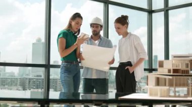 Proje planına bakarken tasarımla ilgili düşünen, paylaşan, beyin fırtınası yapan profesyonel mimar mühendis takımı. Genç bir mimar, genç ve güzel bir menajer not alırken elinde bir plan tutuyor. İzleme