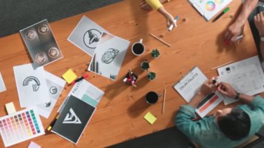 Toplantıda tasarımcı yazma ve logo grafiği tasarlamanın en üst görünümü. Renkli paletler üzerinde çalışan iş adamlarının yakınlaşması ve masaya kağıt ve ekipman ile yapışkan notlar yazmak. Sempozyum.