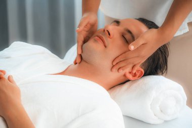 Beyaz adam stres önleyici kafa masajından ve lüks bir tatil beldesi veya otel spa salonundaki modern ışık ortamında yüz güzelliği eğlencelerini şımartmaktan hoşlanıyor. Sessiz.