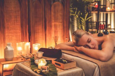 Lüks tatil köyündeki kaplıcalarda sıcak taş masajı, sıcak mum ışığı, spa bazalt taşı masajının keyfini çıkaran mutlu kadın müşteriler, rahatlatıcı bir sıcaklıkla vücudun üzerinde süzülüyorlar. Sessiz.