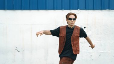 Beyaz arka planda break dans pratiği yapan yakışıklı bir sokak dansçısı. Hip hop tarzı giyinen sporcu, mavi arka planlı bir sokakta müzik eşliğinde ayak sesleri çıkarıyor. Açık hava sporu 2024 hiphop..