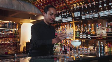 Asyalı barmen karışık kremalı votka bardağı servis ediyor. Önünde buzlu pembe çiçekli şeker, önünde özel içecek, lüks tezgah barında alkolü canlandırıyor. Vinosity.