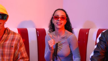 Mutlu kız kameraya bakıyor ve kanepede otururken pop müzik dinliyor. İspanyol kadın serbest stil dans ederken kameraya bakıyor neon ışıkta çeşitli arkadaşlarla dans ediyor. Mutluluk.