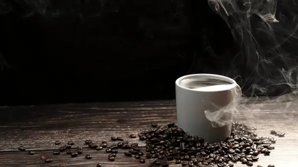 stock image Top view of coffee or espresso with piles of coffee beans. Close up of fresh roasted coffee bean scatter around wooden table with cup of americano and aromatic stream and smoke from seed. Comestible.