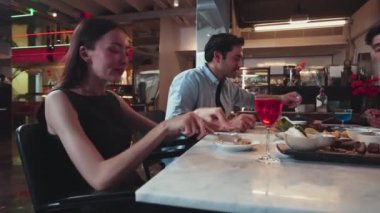 Lezzetli şef sofrasında ana yemeği tatmaya odaklanan güzel bir kadın. Arkadaşları arka tarafta birlikte yemek yiyor. Çiftle ya da arkadaşla restoranda kutlama teması. Vinosity.