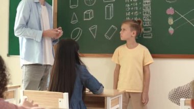Profesyonel öğretmen konuşuyor ve sınıfta Asyalı çocuğa fikrini açıklıyor. Sınıfın önünde karatahta matematik dersiyle dikilmiş beyaz öğrenci dinleme eğitmeni. Pedagoji.