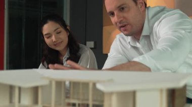 Ev planı çizmek için birlikte çalışan yetenekli mimar mühendisi. Mimar takımı, mimari model, plan ve dizüstü bilgisayarla ofis masasına yerleştirilen ev inşaatı hakkında tartışır. Yönlendirici.