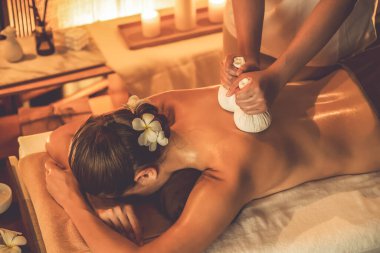 Sıcak bitkisel top spa masaj vücut tedavisi, masör kadın vücuduna nazikçe şifalı bitki torbası bastırıyor. Aromaterapi tesisinin sakinliği ve dinginliği kaplıca salonundaki mumların sıcacık ışığında. Sessiz.