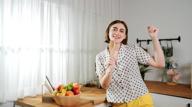 Enerjik beyaz anne kahvaltı için salata pişirirken ve yemek pişirirken elinde kepçeyle şarkı söylüyor. Sağlıklı yemek yapmaya hazırlanırken müziğe yönelen mutlu ev sahibi. Pedagoji.
