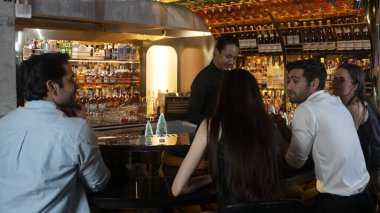 Gülümseyen Asyalı barmen VIP konuğuyla konuşurken süslü Noel ağacı tezgahında karışık kokteyl hazırlıyor. Gece kulübü lüksünde gece hayatını gösteren özel bir içecek. Vinosity.