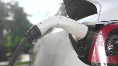 Yavaş çekim EV elektrikli araba yazın yeşil sürdürülebilir şehir bahçesinde şarj oluyor. Kentsel sürdürülebilirlik yaşam tarzı yeşil temiz yeniden şarj edilebilir enerji elektrikli BEV araç iç organları