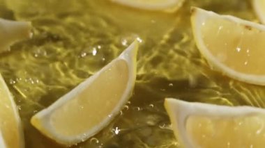Sarı arka planda suya düşen limon dilimlerinin yukarıdan görünüşü. Taze limon dilimlenmiş, ayrı sarı arka planda su dökülüp sıçrama yapılan yere yakın durun. Citrus tazeliği. Pabulum.
