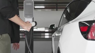 Yavaş çekim adamı, EV elektrikli arabasıyla alışveriş merkezinin otoparkına gidiyor. Şehrin sürdürülebilirlik yaşam tarzını yeşil, temiz, yeniden şarj edilebilir elektrikli araç iç organlarıyla şarj ediyor.