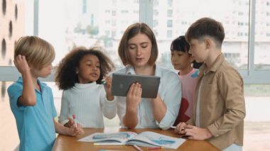 Bir grup öğrenciye çevrimiçi ders verirken elinde tablet tutan akıllı öğretmen. Yetenekli eğitmen mühendislik derslerini anlatırken genç öğrenci oturuyor ve sunumu dinliyor. Etkinlik.