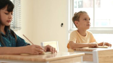 Zeki öğrenci sınıfta otururken öğretmenlerin sorularına cevap verir. Tahtaya bakarak ve ilköğretim sınıfına katılarak çeşitli çocuklar öğreniyor ve öğreniyor. Eğitim konsepti. Pedagoji.