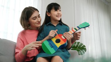 Kafkasyalı bir anne evde akustik müzik öğretirken ukulele çalan mutlu kız. Sevimli çocuk enstrüman öğreniyor. Kafkasyalı mutlu anne ve kız birlikte vakit geçiriyorlar. Pedagoji.