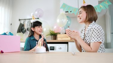 Energetic daughter and mother singing birthday song while clapping hand to music together. Caucasian mom celebrated birthday while using cake at dinning room decorated with colorful balloon. Pedagogy. clipart